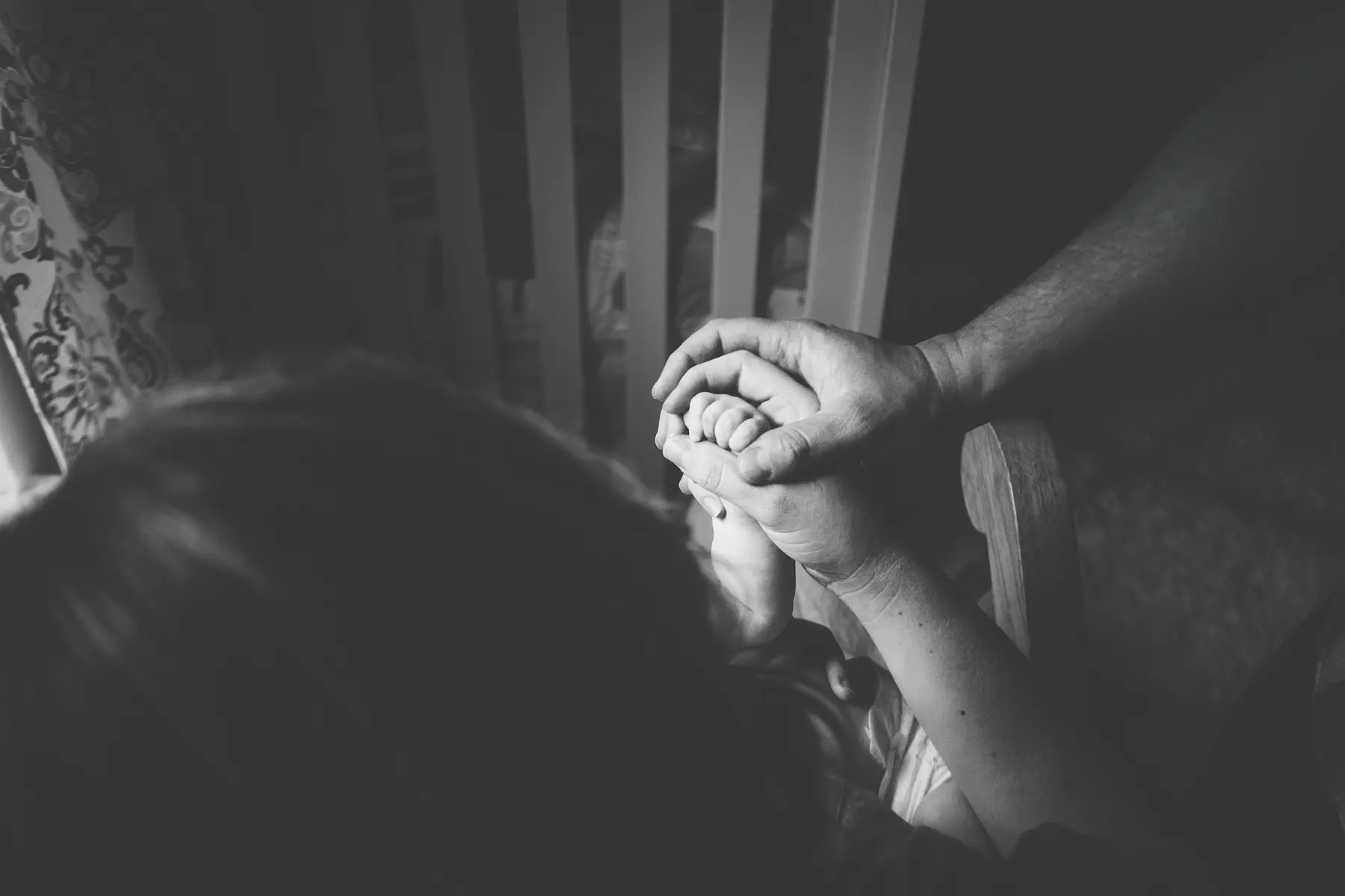 As mãos de um pai e de uma mãe a segurar a mão do bebé.